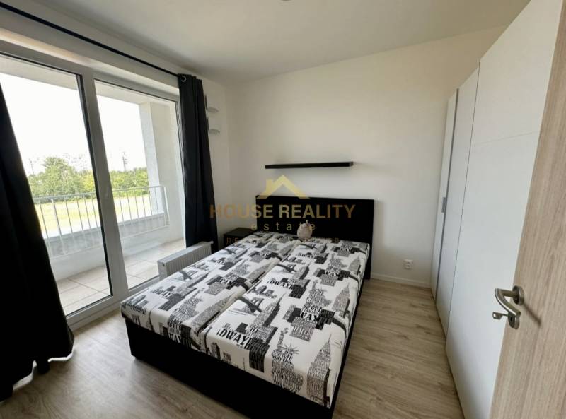 Bedroom in a 2-room apartment with a bed, wardrobe, and balcony with a wooden decor floor.