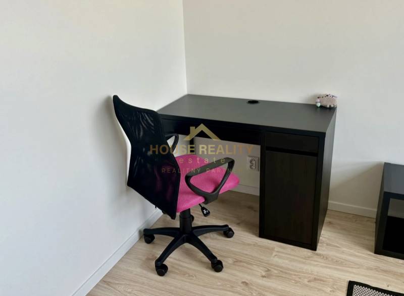 A workspace with a black desk and a pink chair on a wooden-decor floor in a 2-room apartment.