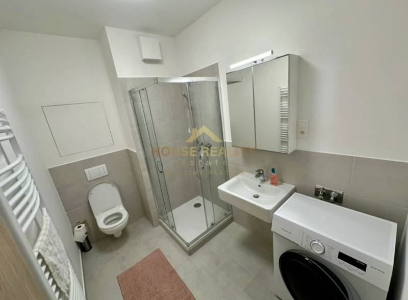 A bathroom with a shower, a sink, and a washing machine in a 2-room apartment.