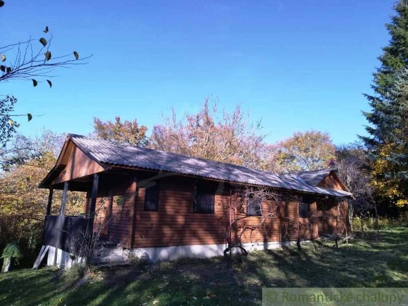A wooden cottage in Dudince surrounded by autumn nature and a blue sky.