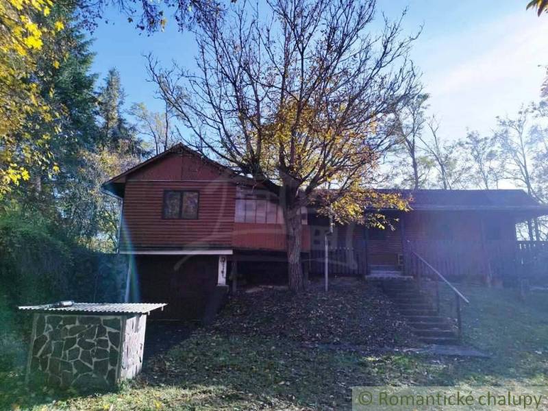 A cottage in Dudince surrounded by trees, with a small stone structure in the garden.