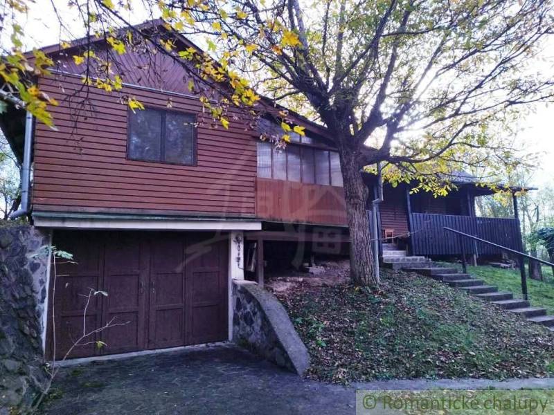 A wooden cottage in Dudince surrounded by trees and a grassy slope.