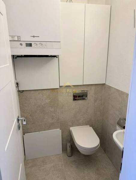 A toilet in a 3-room apartment with a modern wall-mounted boiler and beige tiles.