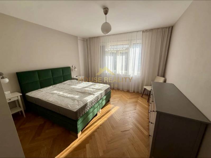 Bedroom with a green bed, wooden decor flooring, opaque curtains, 3-room apartment.