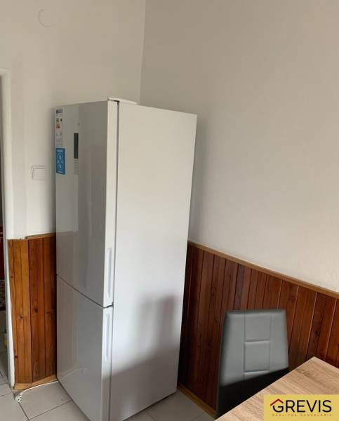 A kitchen in a 2-room apartment with a white refrigerator and wooden wall panels.