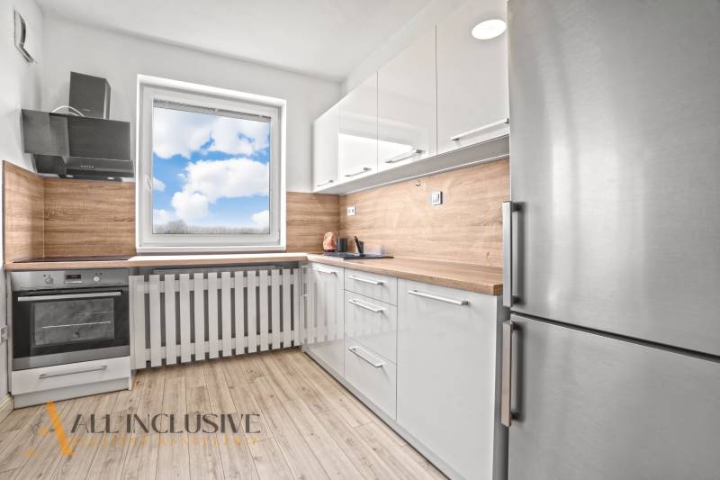 White kitchen in a 2-room apartment with wood-patterned flooring and a view from the window.