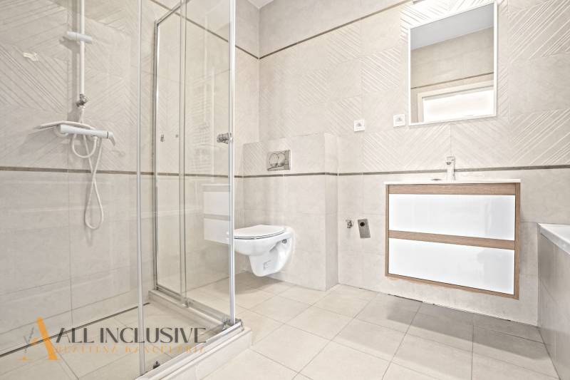 A bathroom in a 2-room apartment with a glass shower enclosure and light tiles.