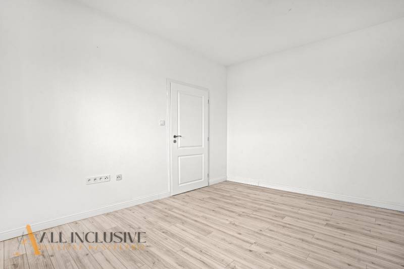 A white room with a wood-patterned floor, white doors, and drawers in a 2-room apartment.