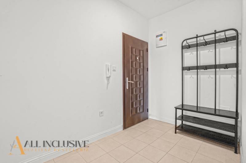 Spacious hallway in a 2-room apartment with tiles and a wall-mounted coat rack.