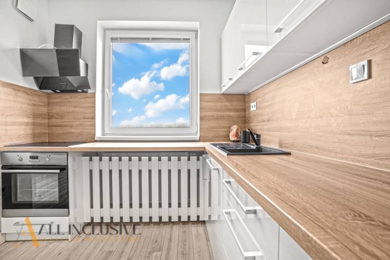 A kitchen in a 2-room apartment with a wood-patterned floor and a view of the sky.
