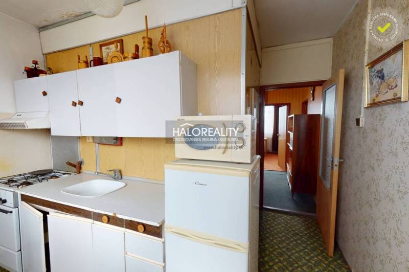 A kitchen in a 3-room apartment with white cabinets and a refrigerator on a floor with a wooden decor.