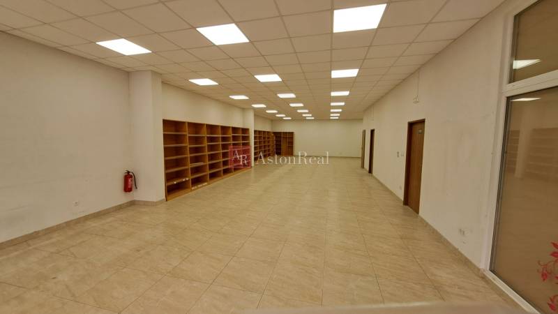 Retail space with shelves, tiles, and a white ceiling with lights.