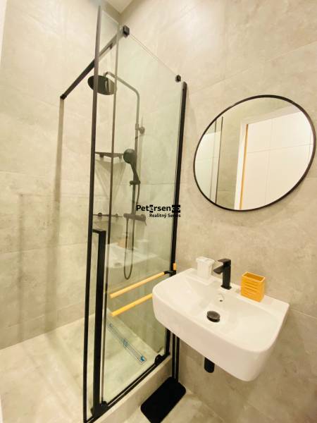 A bathroom in a 2-room apartment with a round mirror, a shower corner, and masonry walls.