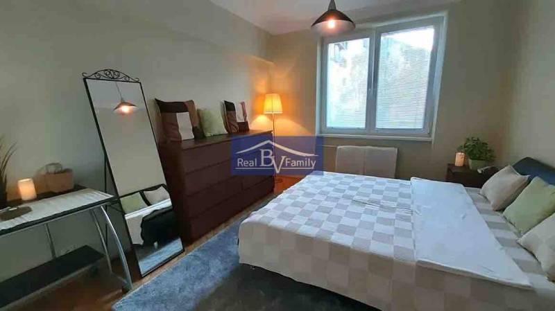 A bedroom in a 2-room apartment with a large mirror and a wooden decor floor.