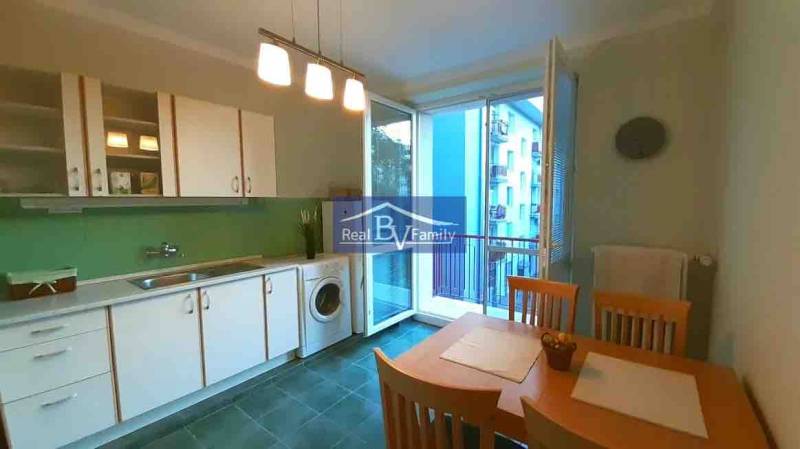 A kitchen in a 2-room apartment with white cabinets, a dining table, and a balcony.