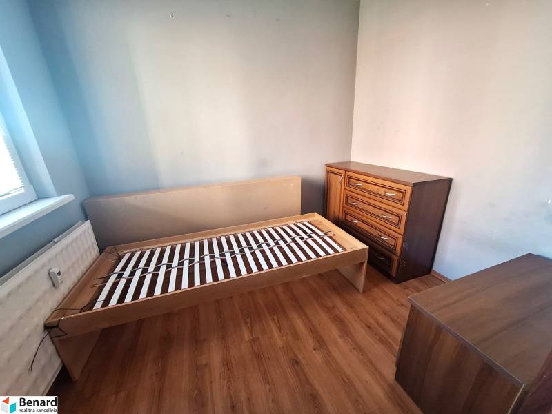 A room in a 3-room apartment with a wooden decor floor, with a bed and a dresser.