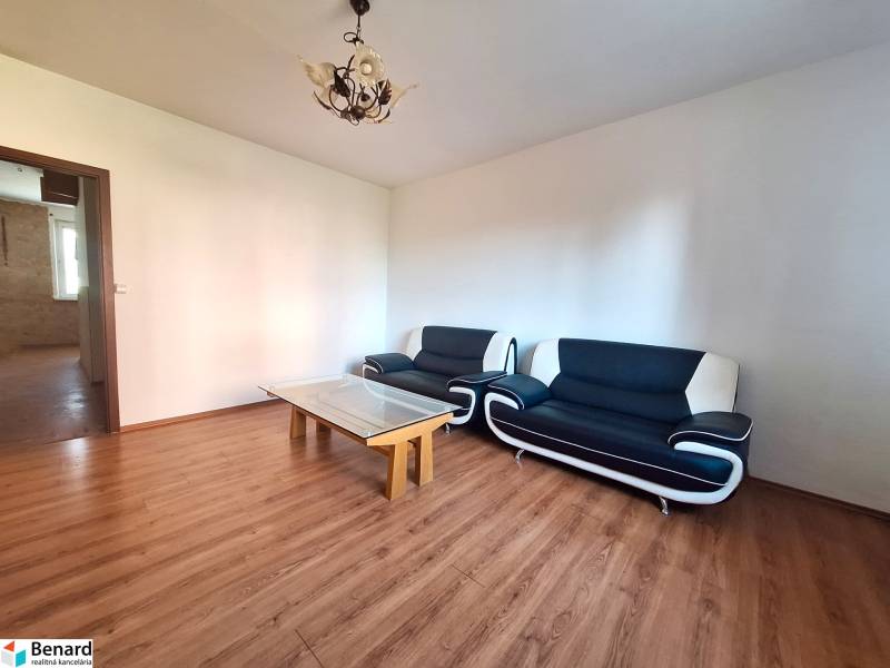 Living room in a three-room apartment with a wooden decor floor and black seating furniture.