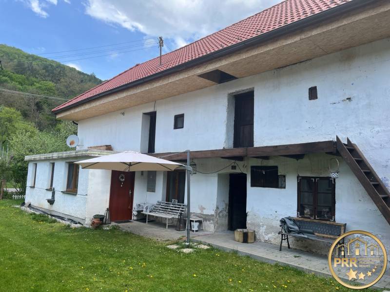 A country cottage with a red roof and a terrace, surrounded by a green lawn and nature.