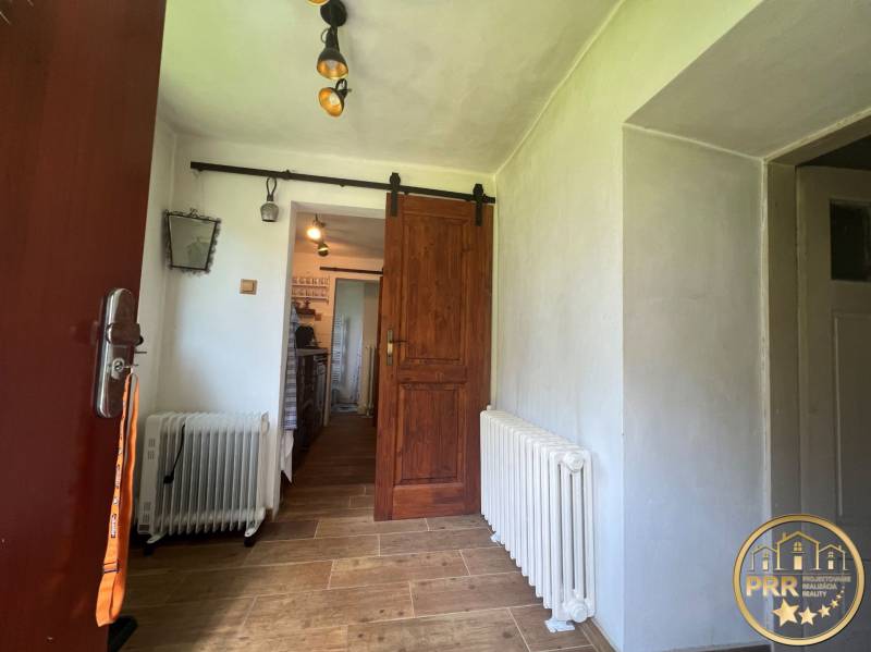 Interior of a cabin with a wood-patterned floor, a radiator, and a sliding wooden door.