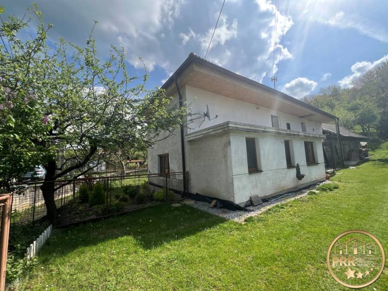 A cottage in Šípkov surrounded by greenery, a fenced garden with trees and a meadow.