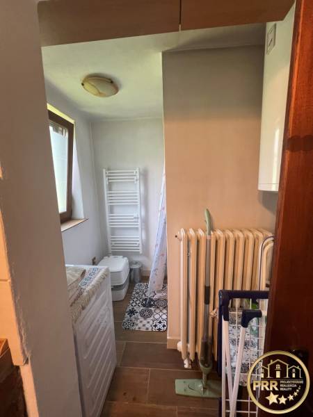 Small bathroom with a washing machine, radiator, and toilet, suitable for a cottage.