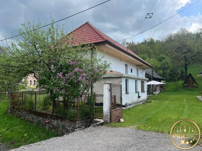 A country cottage surrounded by greenery, with a rustic roof, a blooming garden, and a wooden gazebo.