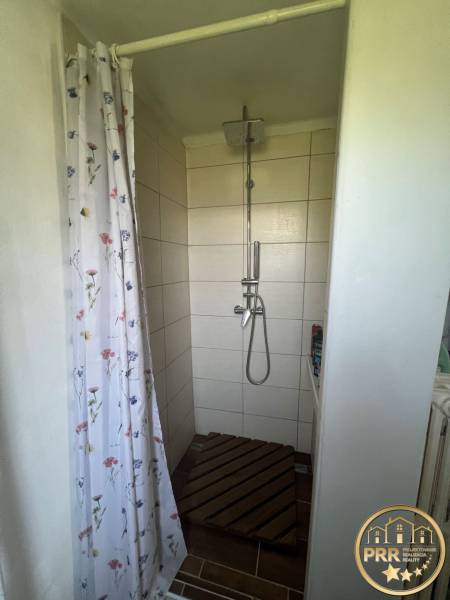 Shower corner with a curtain in a cabin, floor with wooden decor and floral curtain.