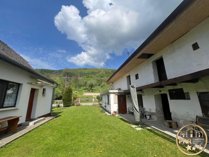 A cottage in Šípkove with a lawn and hilly landscape in the background.