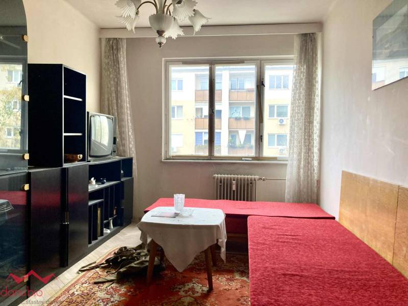 Living room in a 3-room apartment with a red sofa, carpet, older television, bright space.