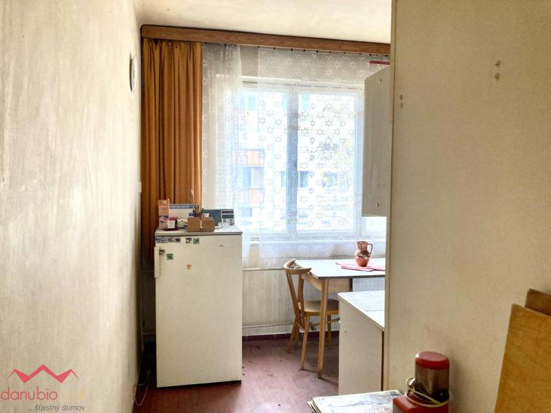 A kitchen in a 3-room apartment with a wooden decor floor, simple furnishings, and a window.