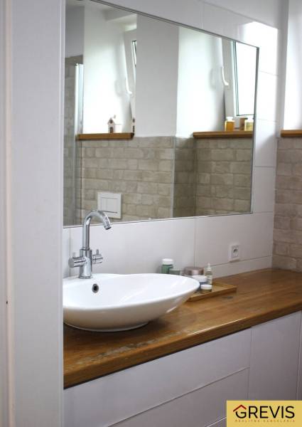 A bathroom with a large mirror and a sink on a wooden decor in a 3-room apartment.
