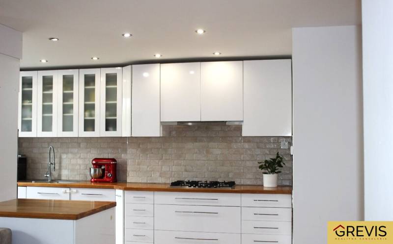A kitchen in a 3-room apartment with white cabinets and a wooden decor countertop.