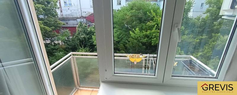 A view from a 3-room apartment with windows and a balcony overlooking a green courtyard.