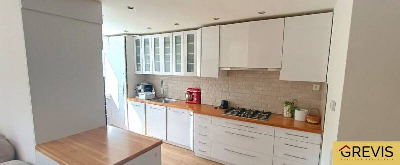 A kitchen in a 3-room apartment with white furniture and a stove, flooring with a wooden decor.
