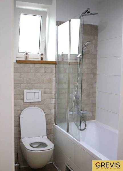 A bathroom in a 3-room apartment with a bathtub, shower, toilet, and a decorative wall in brick decor.
