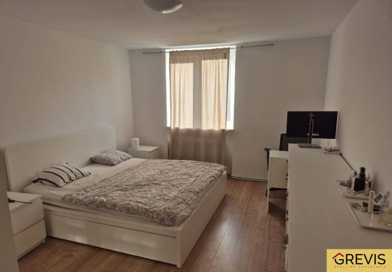 Bright bedroom in a 3-room apartment with a bed and wood-patterned flooring.