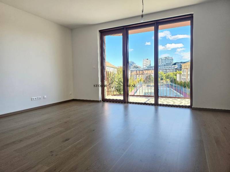 A spacious room with a wooden decor floor and a large window in a studio apartment.