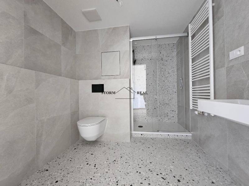 A bathroom in a studio apartment with modern furnishings, a shower enclosure, and large-format tiles.