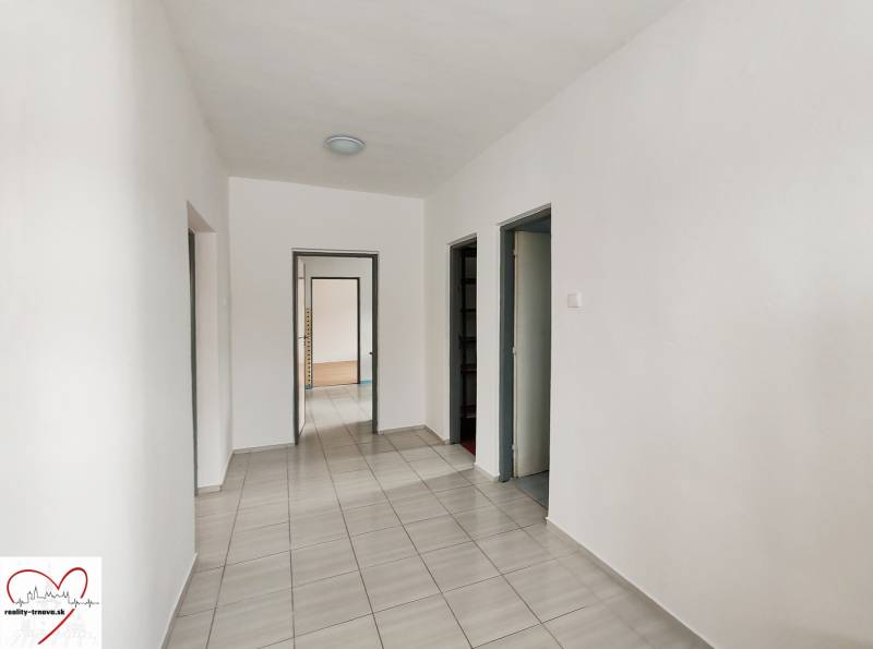 A hallway of a family house with tiles and white walls leading to a door.