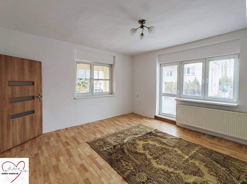 A room in a family house with a wooden decor floor, a carpet, and a large window.