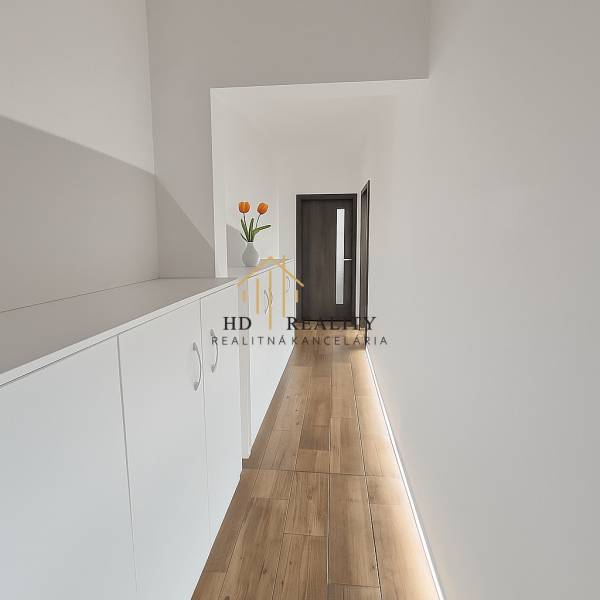 A narrow corridor with white furniture and decoration, a floor with a wooden decor in a 3-room apartment.