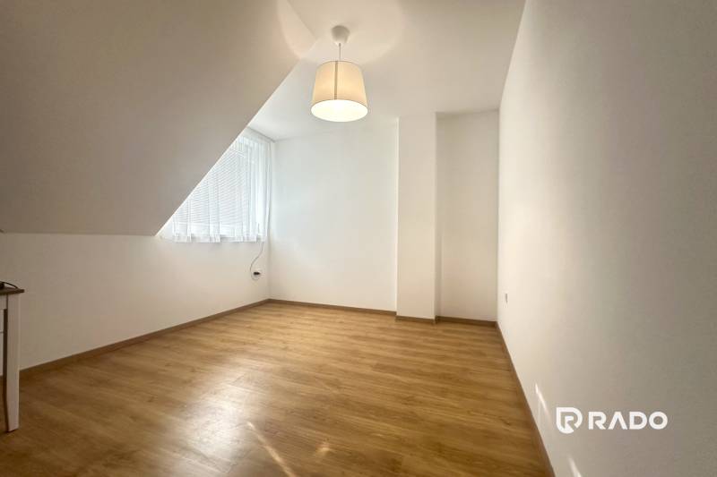 A room in a family house with a wood-patterned floor, a simple lamp, and a large window.