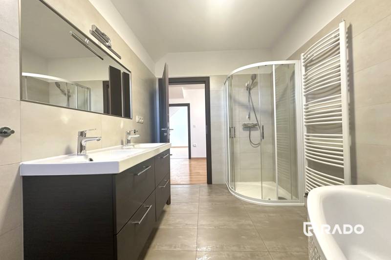 A bathroom in a family house with a double sink, a shower corner, and a wooden decor floor.