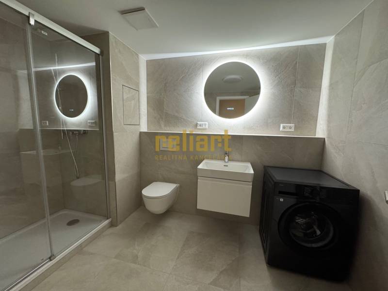 Bathroom with toilet in a 2-room apartment with a washing machine and shower, backlit mirror.