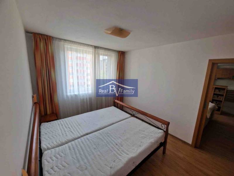 Bedroom in a 2-room apartment with a bed, curtains, and a wooden decor floor.