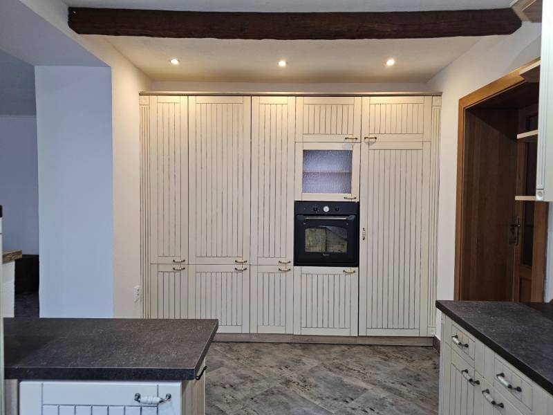 A kitchen with a dark countertop and a built-in oven, floor with wood decor.