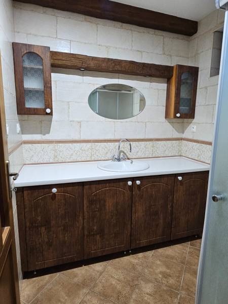 A bathroom in a family house with wooden cabinets, an oval mirror, and ceramic tiles.