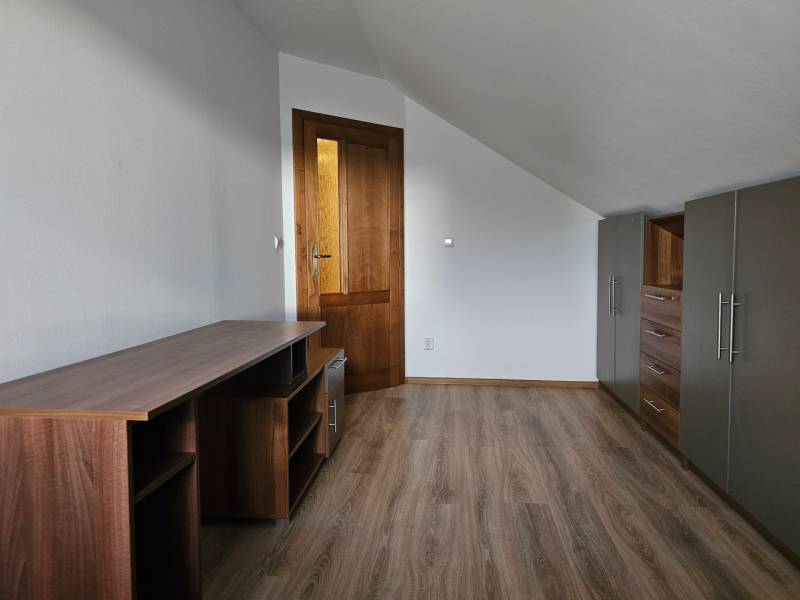A room in a family house with furniture, white walls, and a wood-patterned floor.