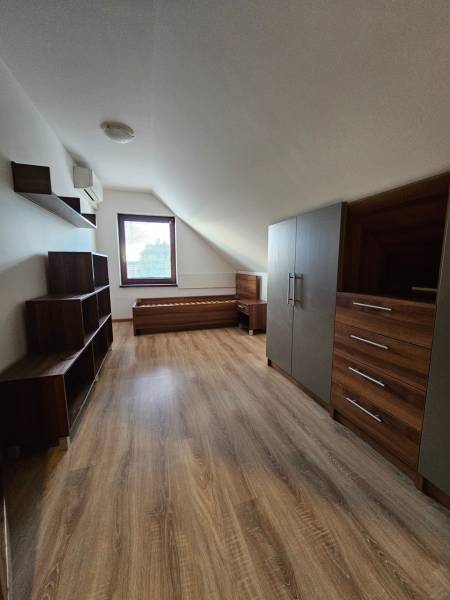 Attic of a family house with furniture, wood-patterned flooring, and a window.
