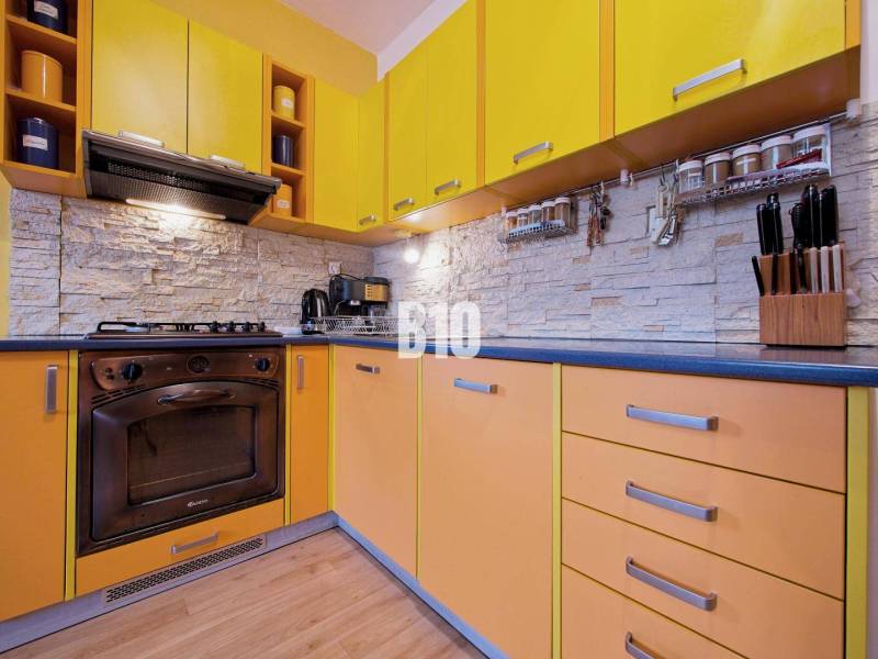 A kitchen in a 2-room apartment with a colorful kitchen unit and a wooden decor floor.